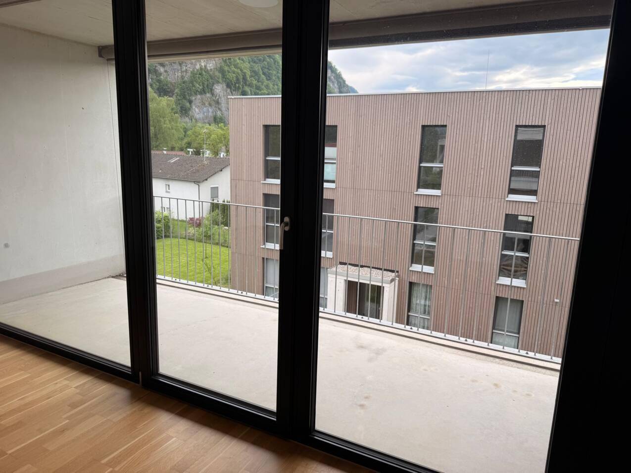 Blick aus dem Innenraum durch große Fenster auf einen Balkon und die umliegende Berglandschaft.