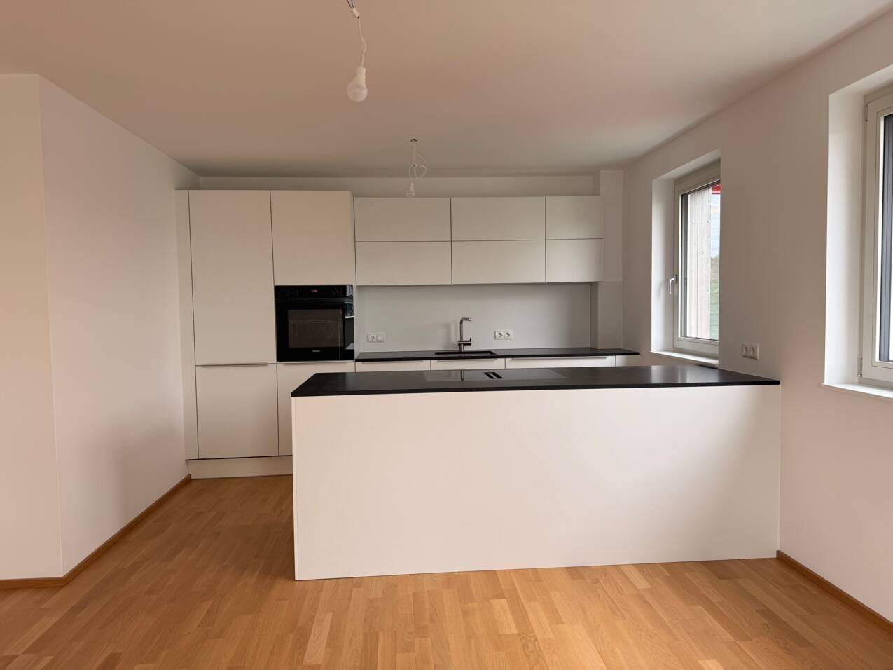 Moderne, unmöblierte Küche mit weißen Schränken, schwarzer Arbeitsplatte und Kücheninsel.