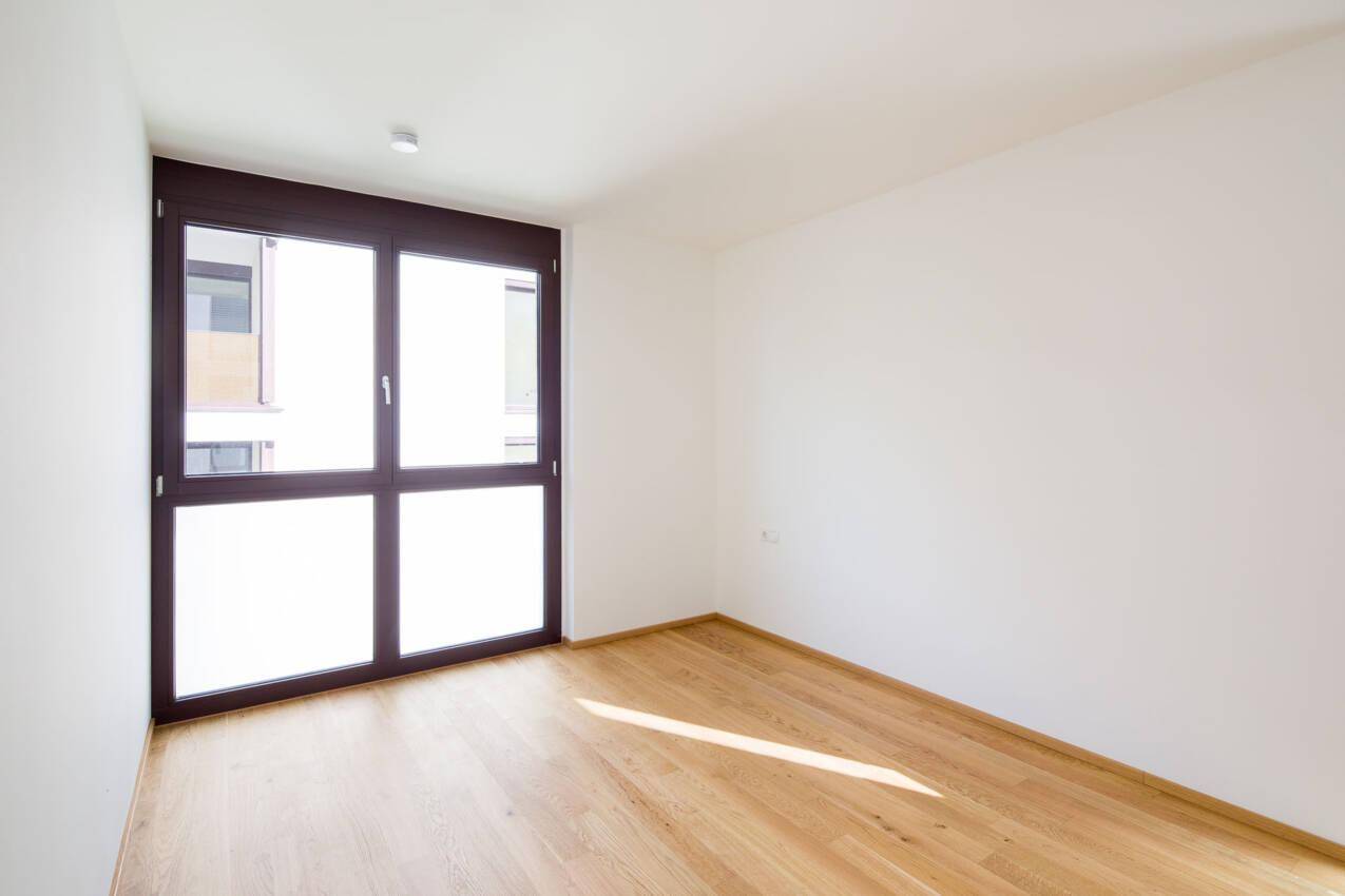 Freundliches Zimmer mit hellem Eichenparkett und großem Fenster, ideal als Schlaf- oder Arbeitszimmer.
