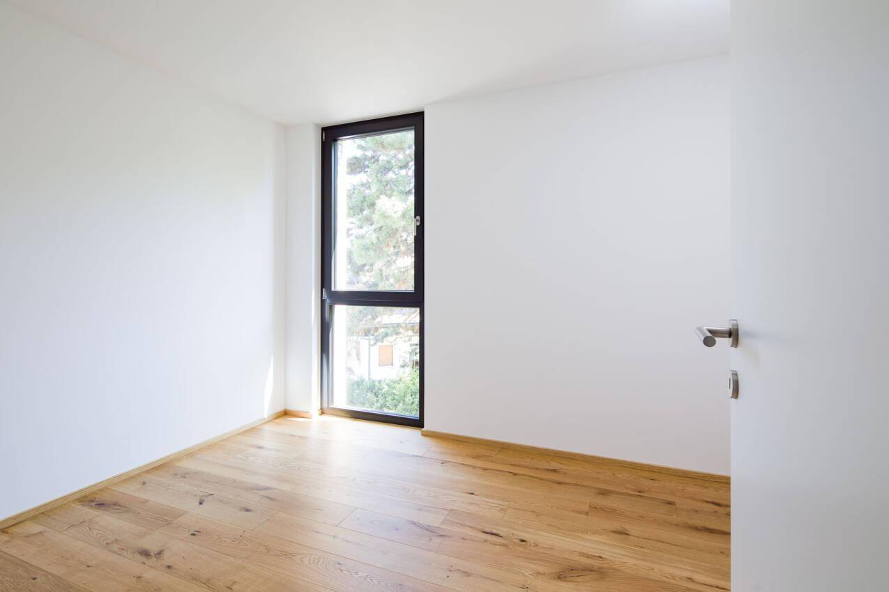 Leerer Raum mit hellem Echtholzboden und einem hohen Fenster für viel Tageslicht.