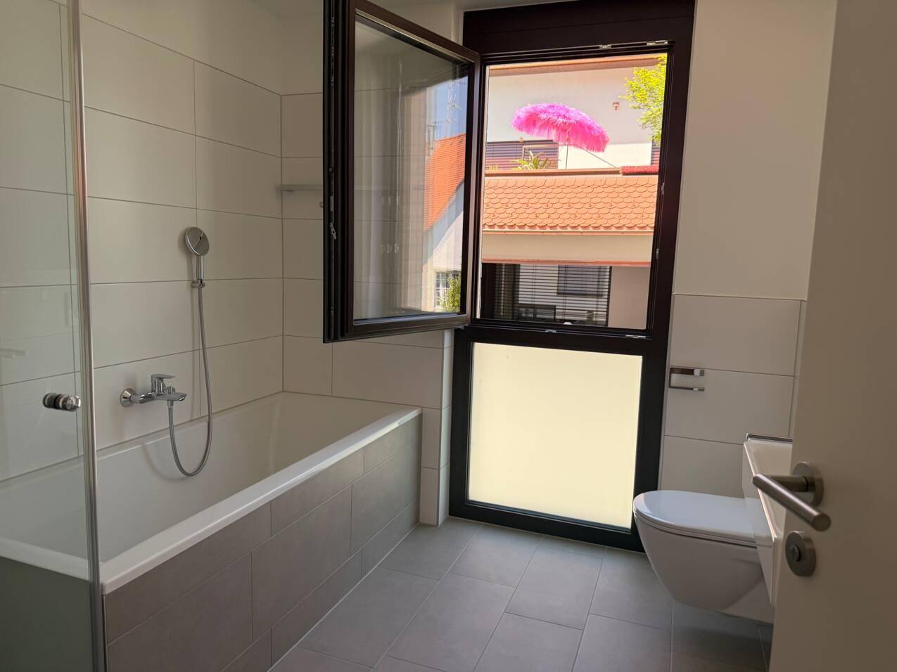 Modernes Badezimmer mit Badewanne, Duschfunktion, wandhängendem WC und großem Fenster für viel Tageslicht.