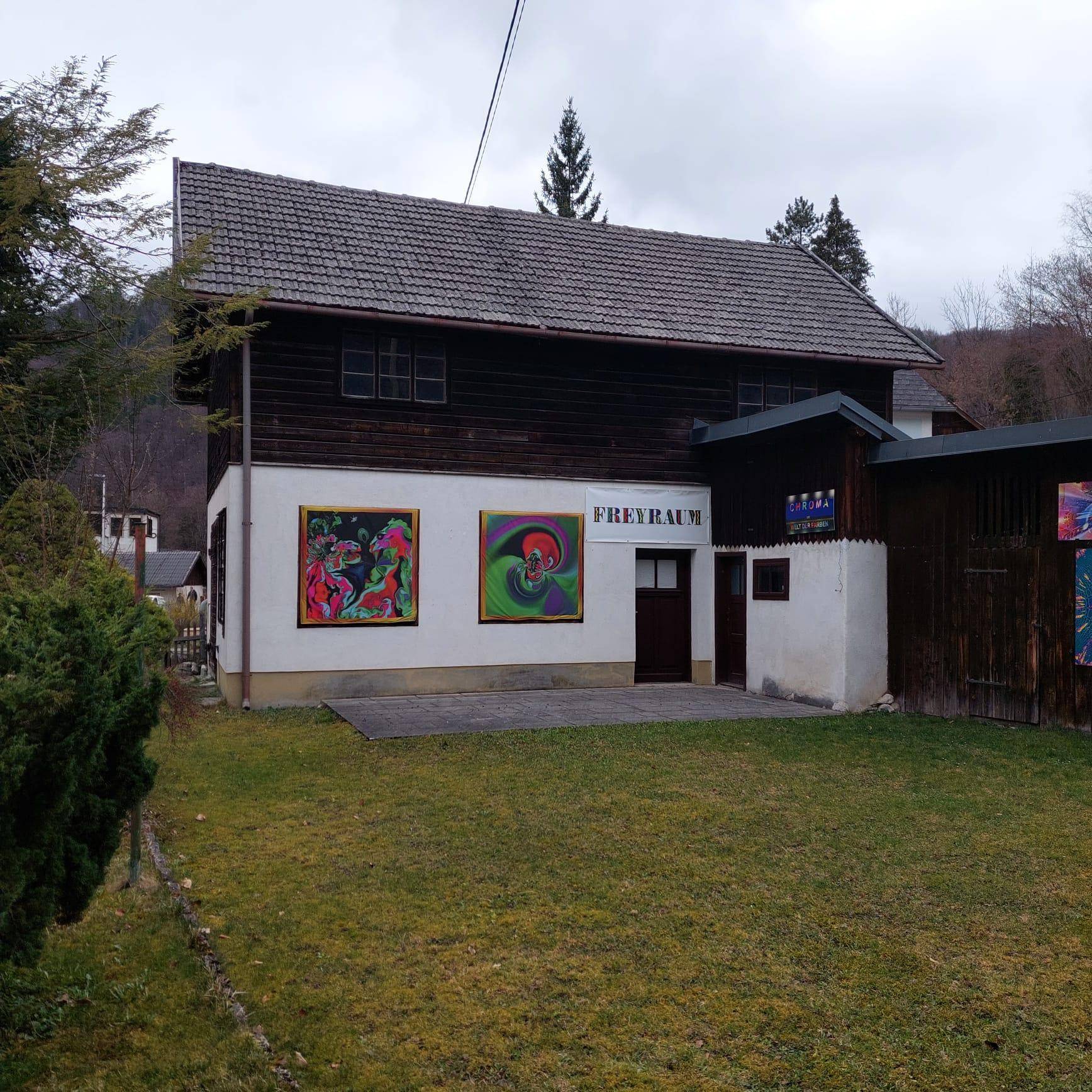 Ansicht eines Nebengebäudes mit Holzelementen und farbenfrohen Kunstwerken an der Fassade.