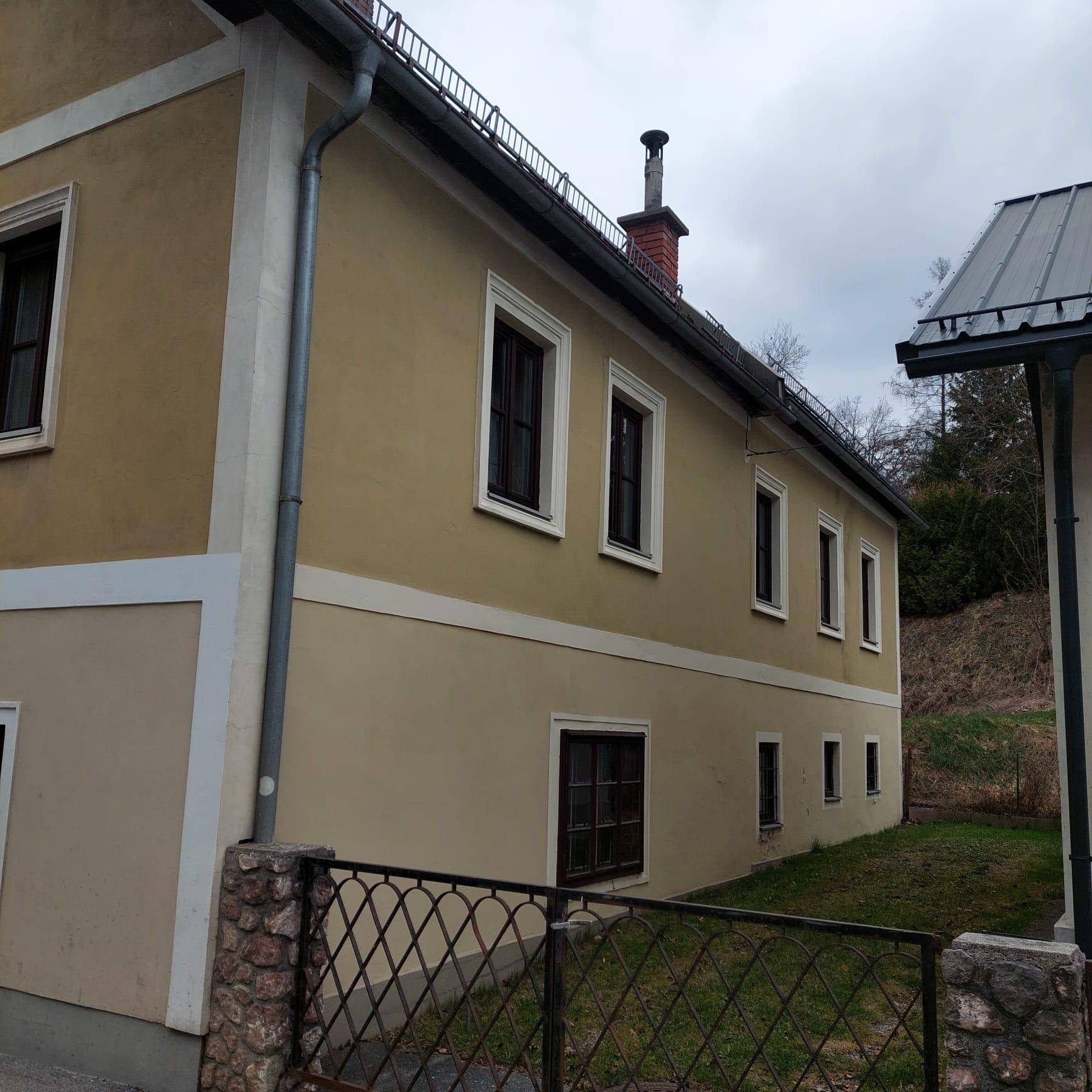 Seitenfassade des Gebäudes mit Regenrinnen und einem Schornstein unter bewölktem Himmel.