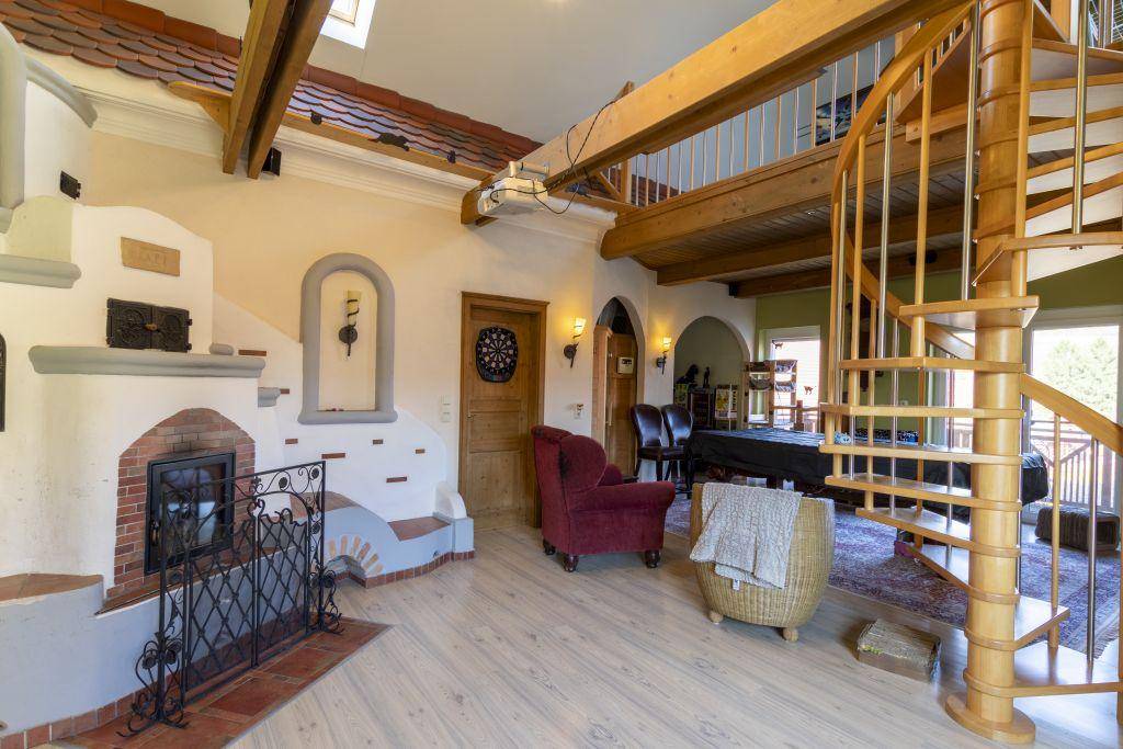 Geräumiges Wohnzimmer mit Wendeltreppe, sichtbaren Holzbalken und einem rustikalen Kaminbereich.