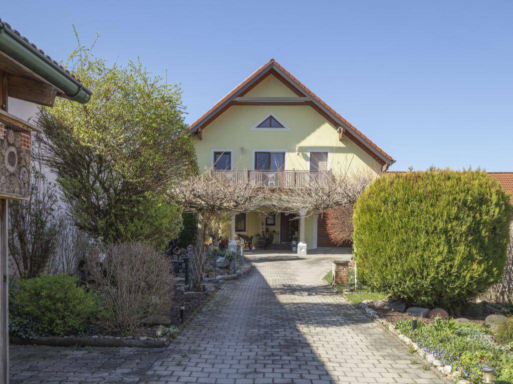 Vorderansicht des Hauses mit gepflasterter Auffahrt, umranktem Eingangsbereich und gepflegtem Vorgarten.