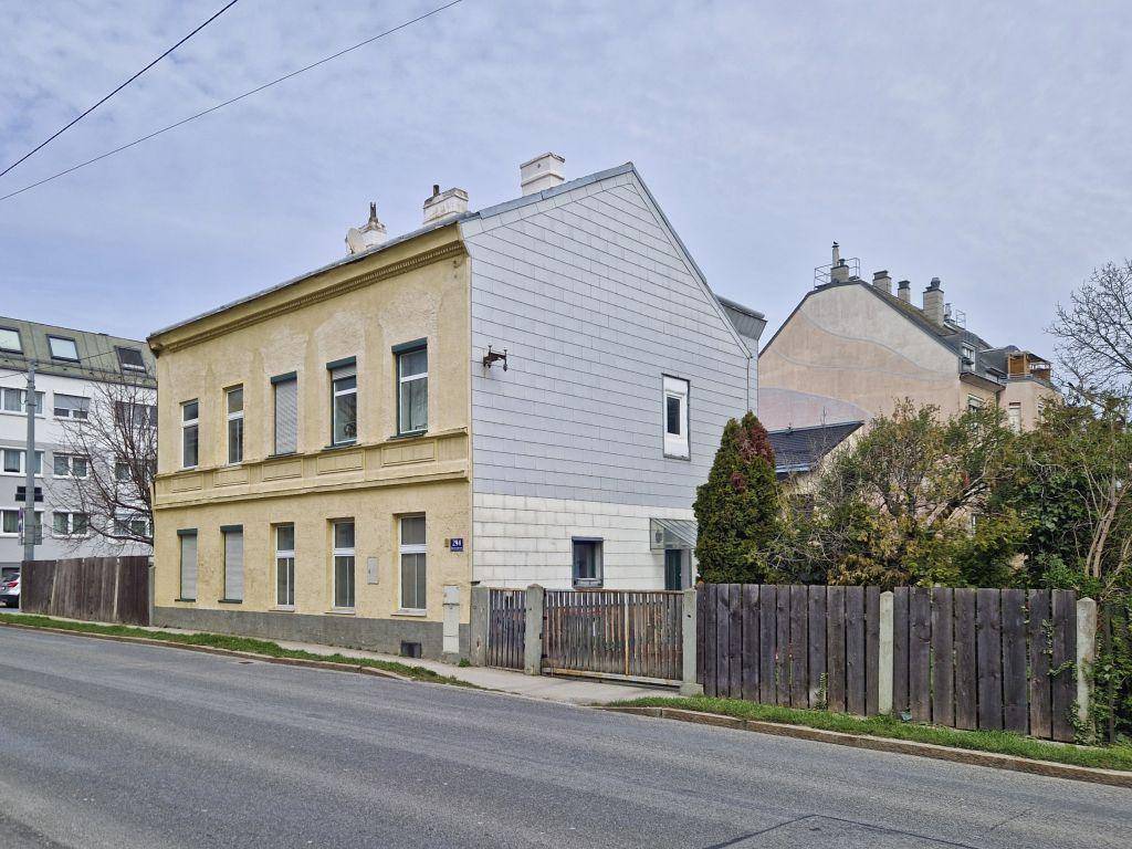 Gelbes Gebäude mit einer modernen grauen Seitenfassade und Holzzaun an der Straße.