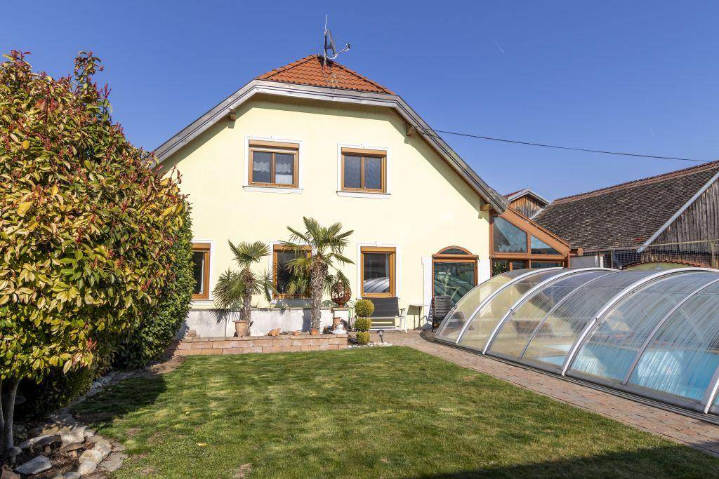 Seitenansicht des Hauses mit Rasenfläche, Palmen und einem überdachten Swimmingpool im Garten.