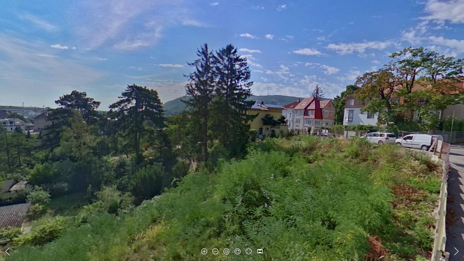 Panoramablick über eine hügelige Wohngegend mit üppiger Vegetation und Häusern entlang einer Straße.
