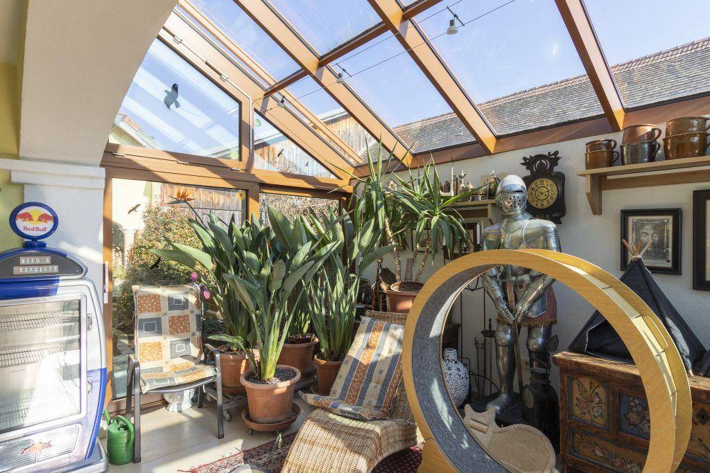 Heller Wintergarten mit Glasdach, vielen Pflanzen und gemütlicher Einrichtung für entspannte Stunden.