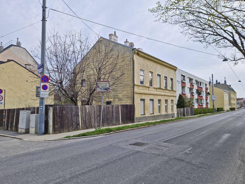 Gelbes Mehrfamilienhaus an einer Straße mit Holzzaun und umliegenden Gebäuden.