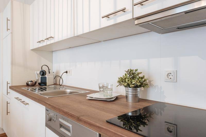Moderne Einbauküche mit weißen Schränken, Holz-Arbeitsplatte und integrierten Geräten.