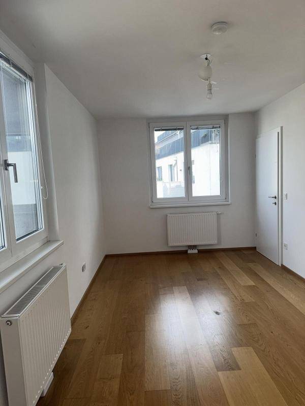 Heller Raum mit Holzboden, weißen Wänden und einem Fenster, das einen Blick nach draußen bietet.