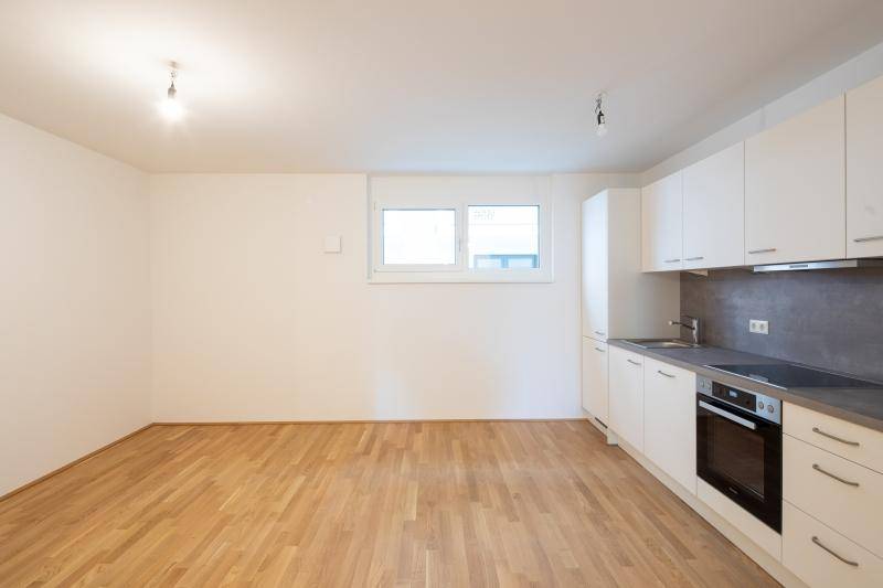 Helle, offene Küche mit weißen Schränken, Holzboden und Fensterblick nach draußen.