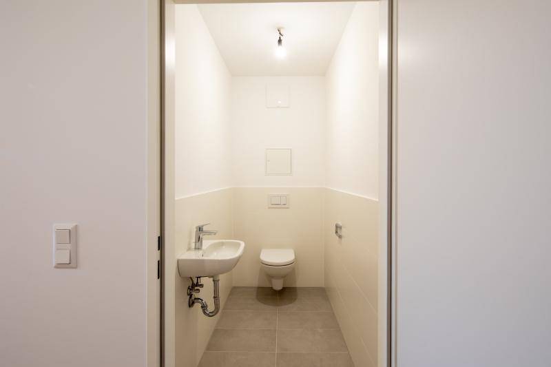Modernes Gäste-WC mit Wand-WC, kleinem Waschbecken und hellen Fliesen.