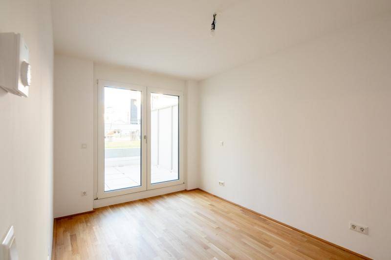 Helles Zimmer mit Holzboden und großen Fenstertüren, die Zugang nach draußen bieten.