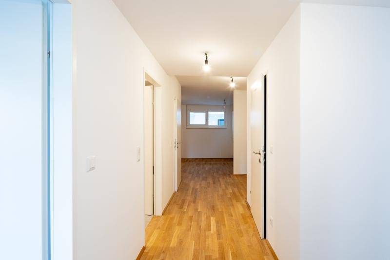 Langer, heller Flur mit Holzboden, weißen Wänden und Türen zu verschiedenen Zimmern.