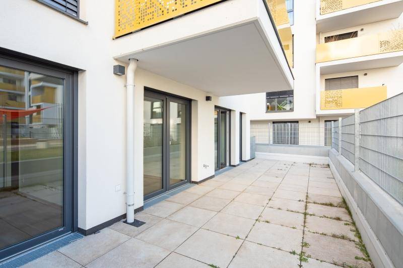 Helle Terrasse mit Fliesenboden und mehreren Fenstertüren, die zum Gebäude führen.