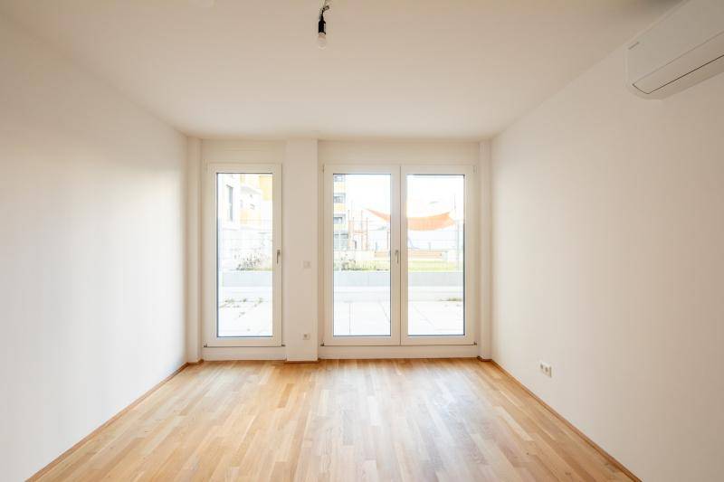Lichtdurchflutetes Zimmer mit Holzboden, mehreren Fenstertüren und Klimaanlage.