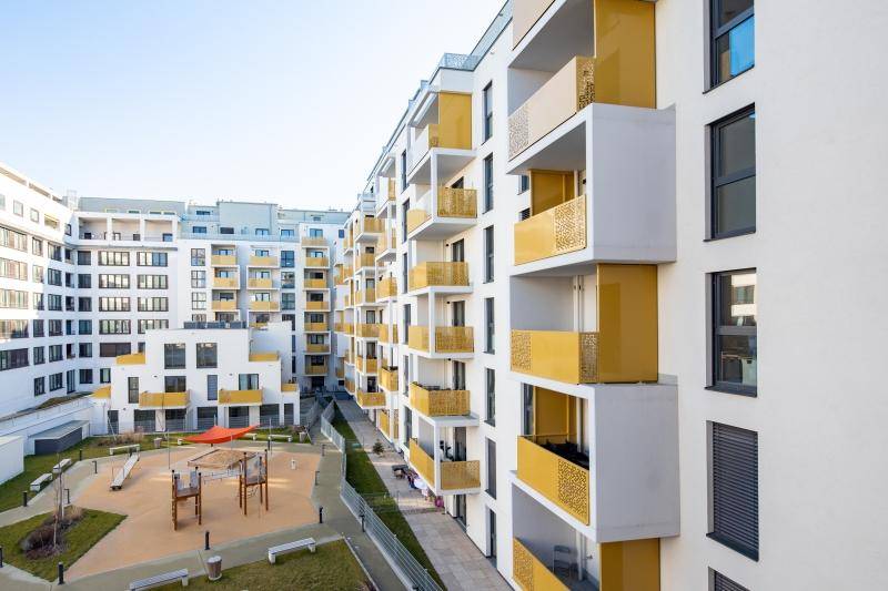 Moderne Wohnanlage mit weißer Fassade, gelben Balkonen und einem Spielplatz im Innenhof.