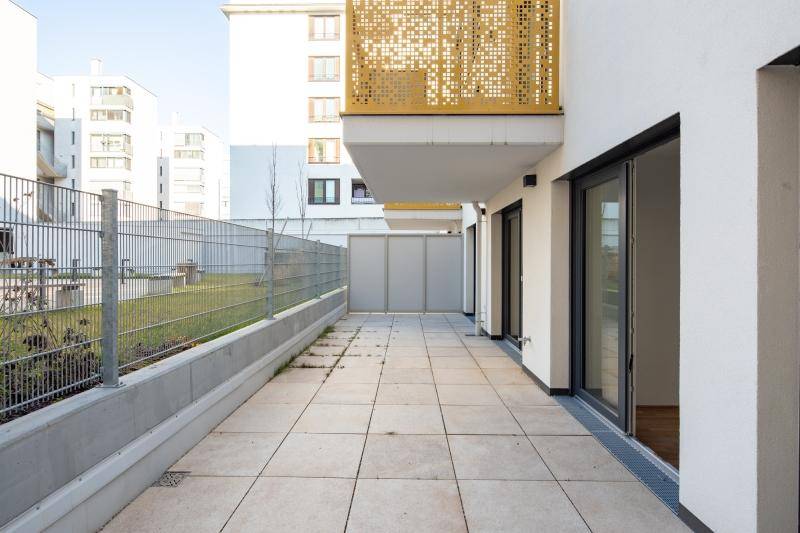 Geräumige Terrasse mit Fliesenboden und angrenzender Rasenfläche, umgeben von einem Zaun.
