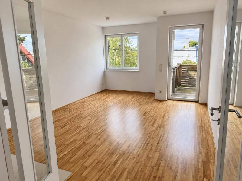 Heller Raum mit Holzboden, Fenster und Zugang zu einem Außenbereich.
