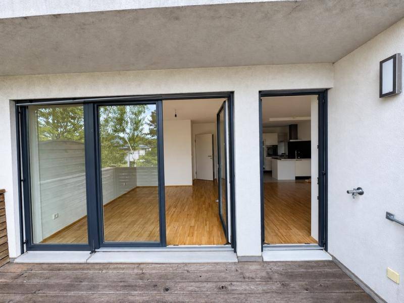 Außenbereich mit Holzboden und großen Glasschiebetüren, die in die Innenräume führen.