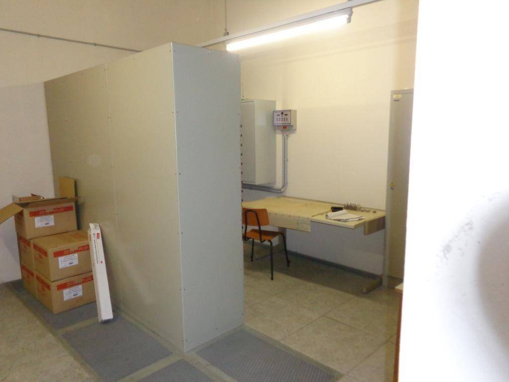Ein einfacher Raum mit einem Schreibtisch, Stuhl und Lagerboxen, beleuchtet von einer Deckenleuchte.