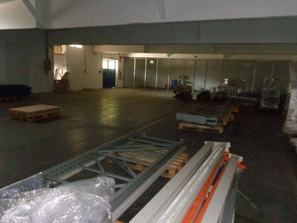 Große, leere Lagerhalle mit Betonboden und einigen Paletten sowie Regalteilen im Vordergrund.