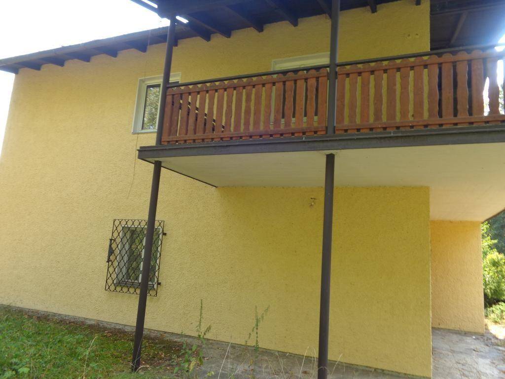 Gelbe Gebäudefassade mit einem Holzbalkon und vergitterten Fenstern, umgeben von Bäumen.