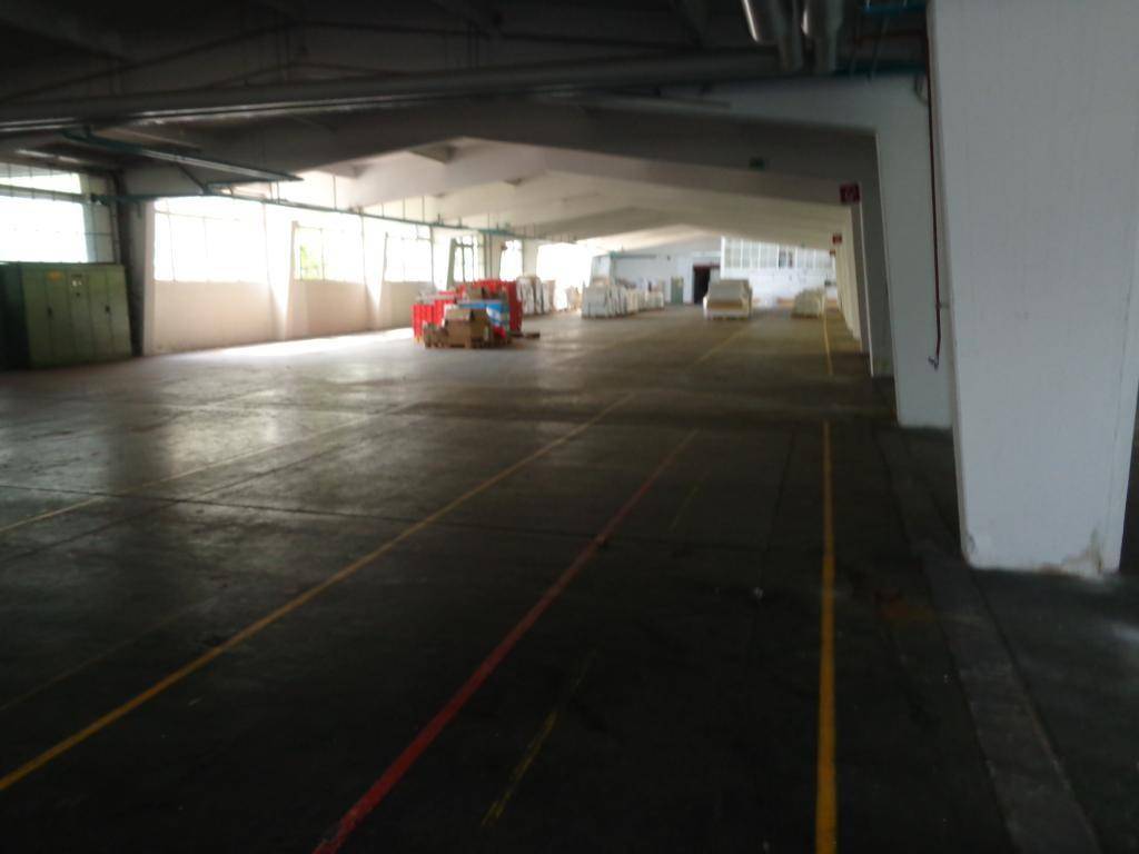 Große Lagerhalle mit hohen Decken, Betonboden und einigen gelagerten Materialien im Hintergrund.