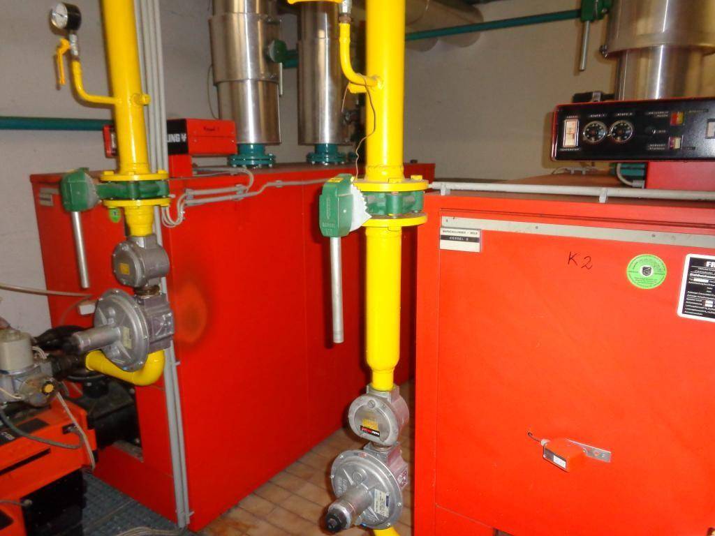 Heizungsraum mit mehreren roten Heizkesseln und gelben Rohren, die die Anlage versorgen.