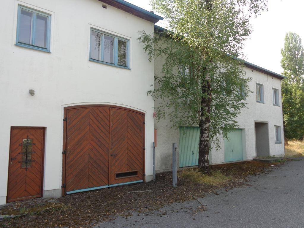 Weiße Gebäudefassade mit großen Holztoren und kleineren Garagentoren, umgeben von Bäumen.