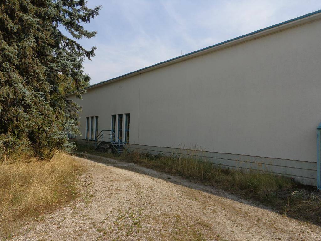 Lange, schlichte Gebäudefassade mit mehreren Türen und einer Treppe, umgeben von Bäumen und Gras.