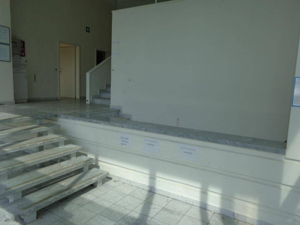 Heller Eingangsbereich mit Treppen, einer Rampe und Fliesenboden, der zu weiteren Räumen führt.