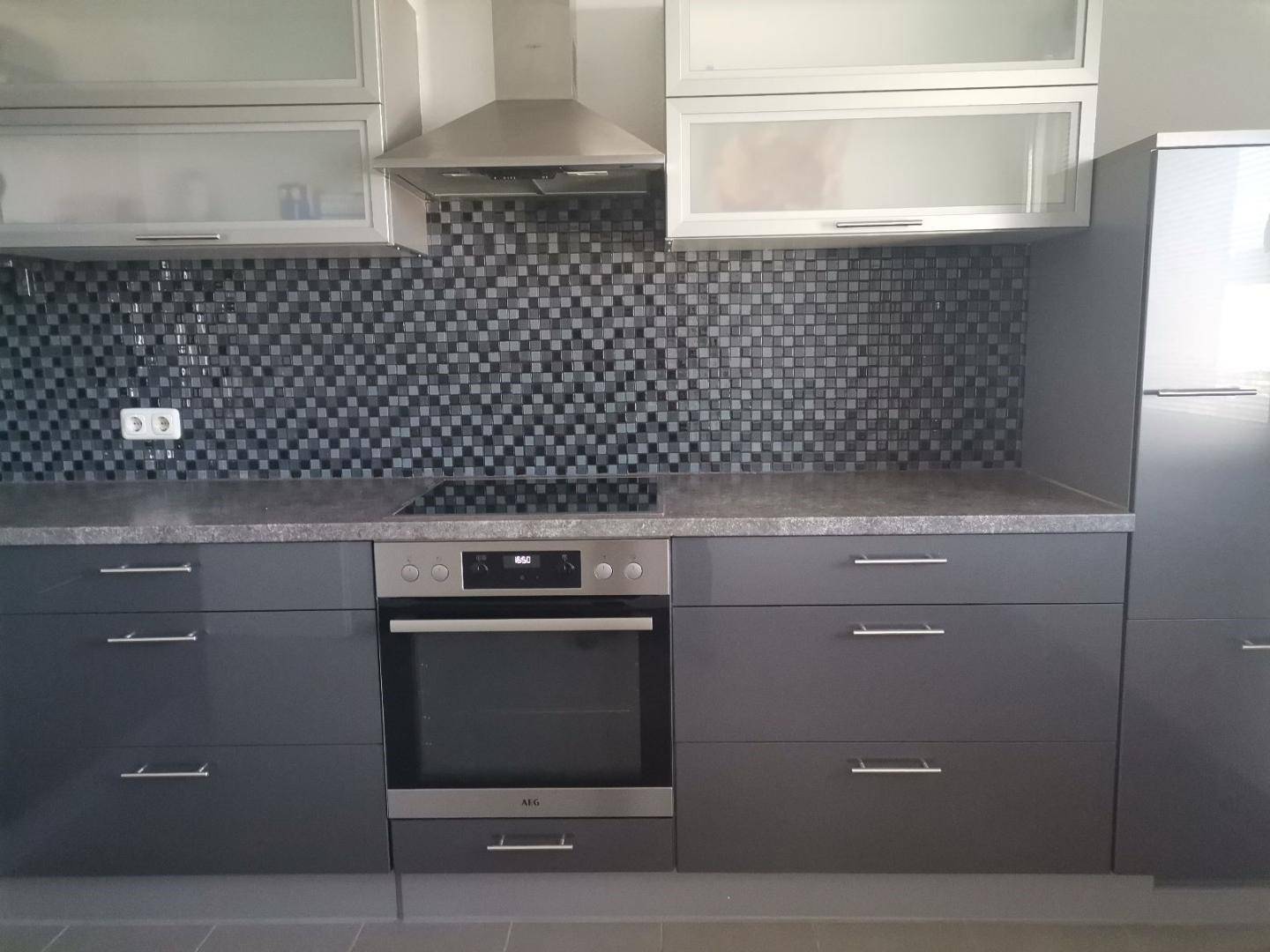 Detailansicht der modernen Küche mit Induktionskochfeld, Backofen und Dunstabzugshaube in Grau.