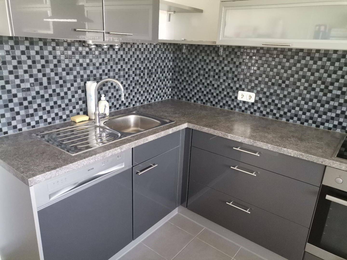 Küchenzeile mit Spülbecken, Geschirrspüler und Arbeitsplatte in Granitoptik, umgeben von Mosaikfliesen.
