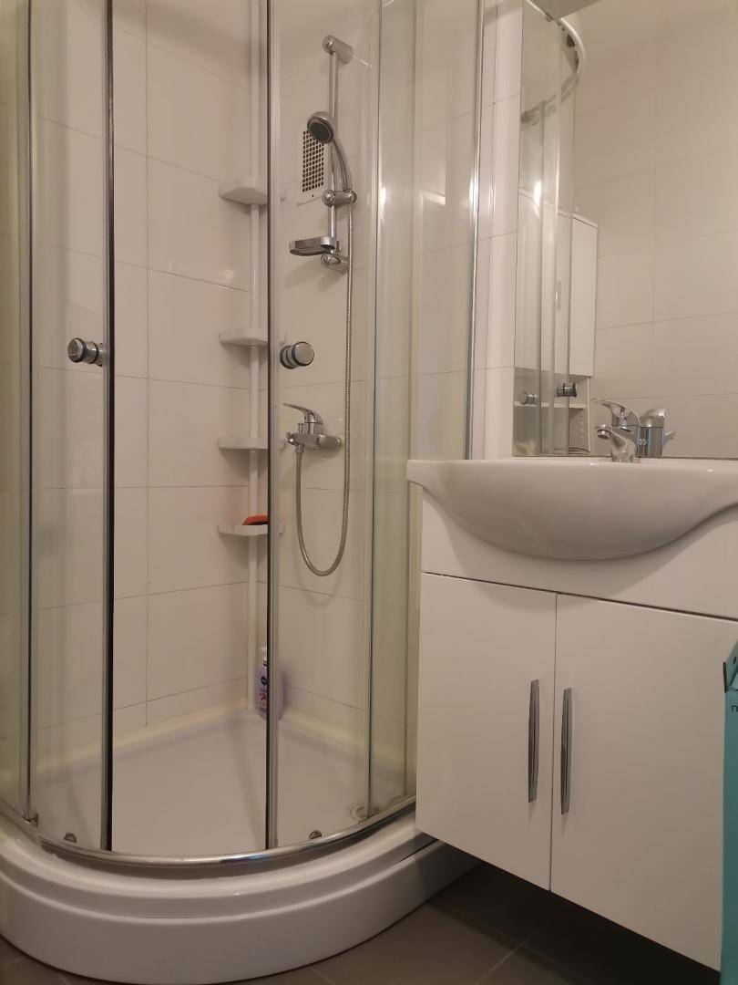Badezimmer mit Duschkabine, weißem Waschbeckenunterschrank und hellen Wandfliesen, funktional gestaltet.