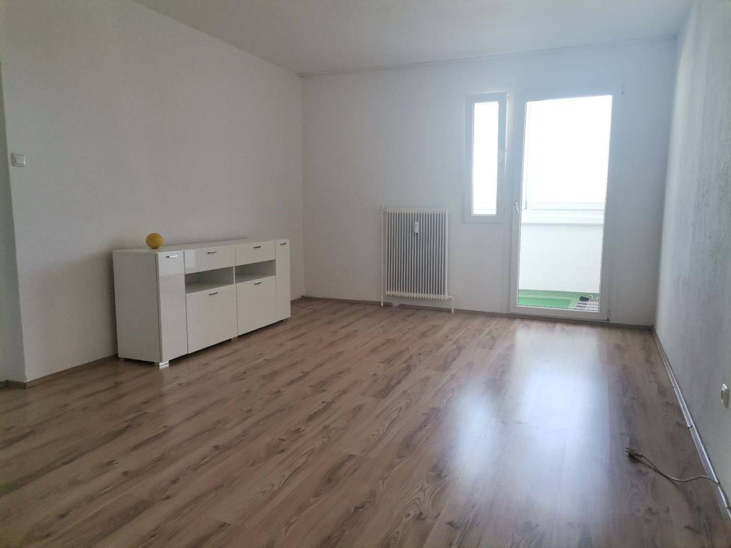 Helles Wohnzimmer mit Laminatboden, weißer Kommode und direktem Zugang zu einem Balkon.