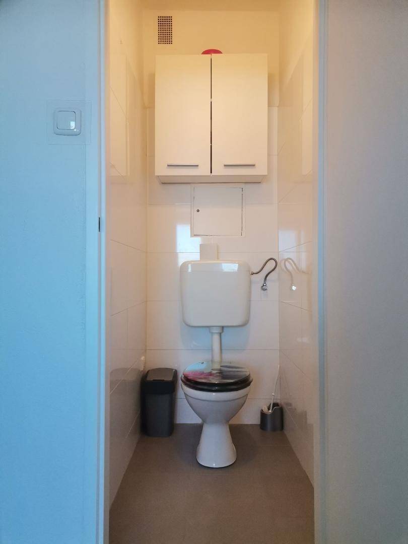 Separates WC mit Toilette, Spülkasten und einem kleinen Wandschrank, praktisch eingerichtet.