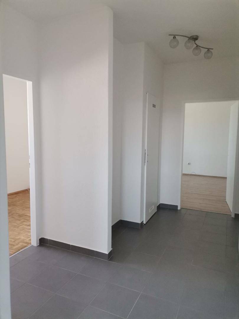 Heller Flur mit grauen Fliesen und Zugang zu verschiedenen Zimmern der Wohnung, gut beleuchtet.
