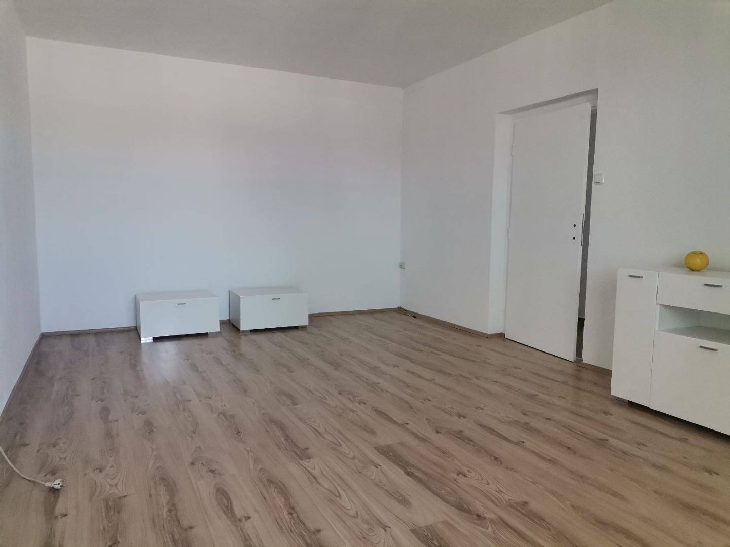 Geräumiges Wohnzimmer mit hellem Laminatboden und weißen Wänden, bereit zur individuellen Einrichtung.