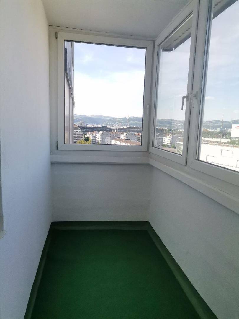 Kleiner Balkon mit Stadtblick und grüner Bodenfläche, ideal für eine gemütliche Auszeit.