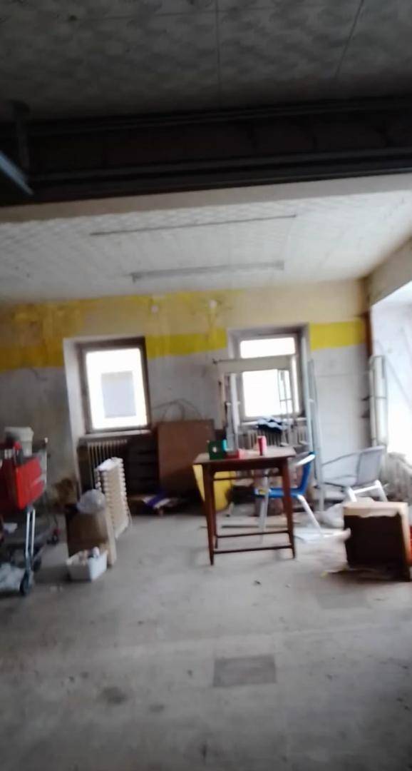 Ein leerstehender Gewerberaum mit abgenutzten Wänden, Fenstern und einem Betonboden, der Renovierung benötigt.