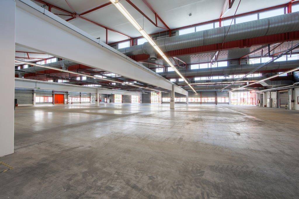 Große Lagerhalle mit Betonboden, roter Stahlkonstruktion und breiten Trägern.
