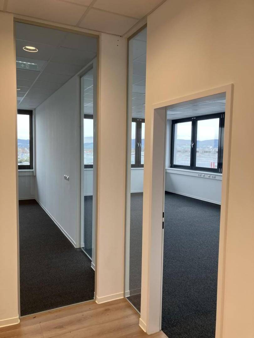 Büroflur mit Laminatboden und Einblicken in helle Büroräume durch Glastrennwände.