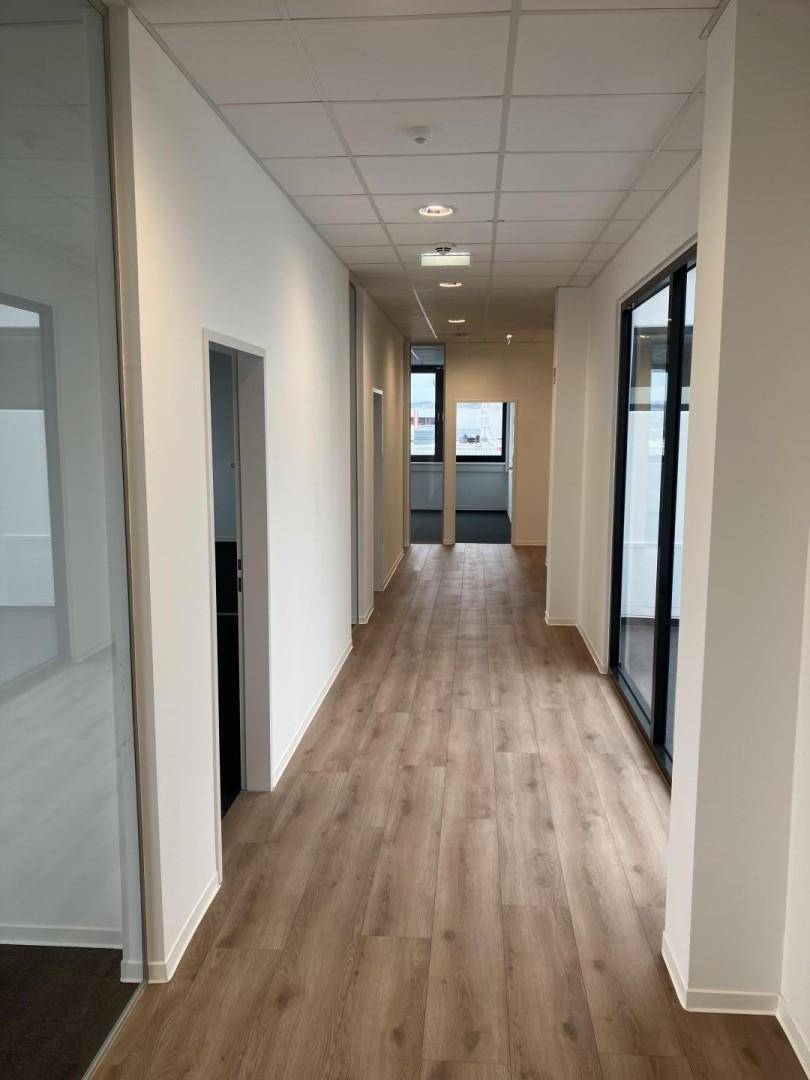 Heller Büroflur mit Laminatboden und Glastüren zu den einzelnen Büroräumen.