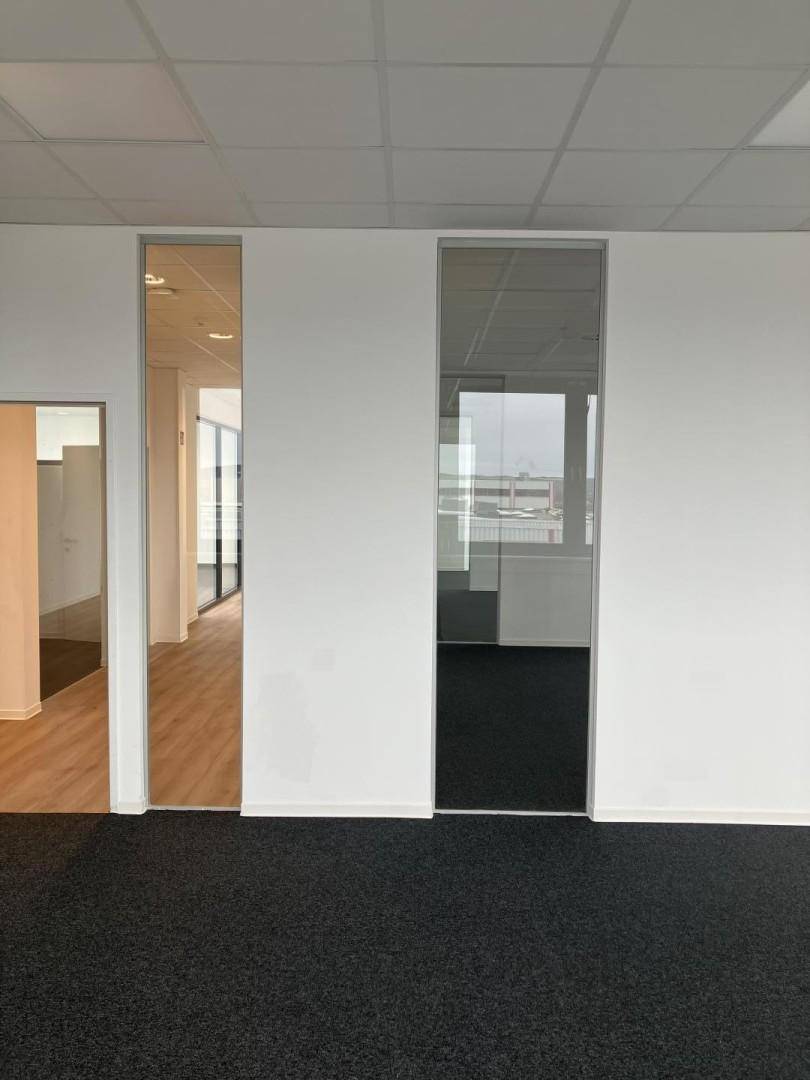 Büroraum mit weiß gestrichenen Wänden und einer Glaswand, die Licht hereinlässt.