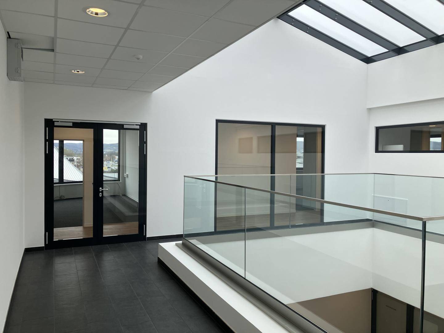 Moderner Flur in einem Bürogebäude mit Glasgeländer und Oberlicht für viel Tageslicht.