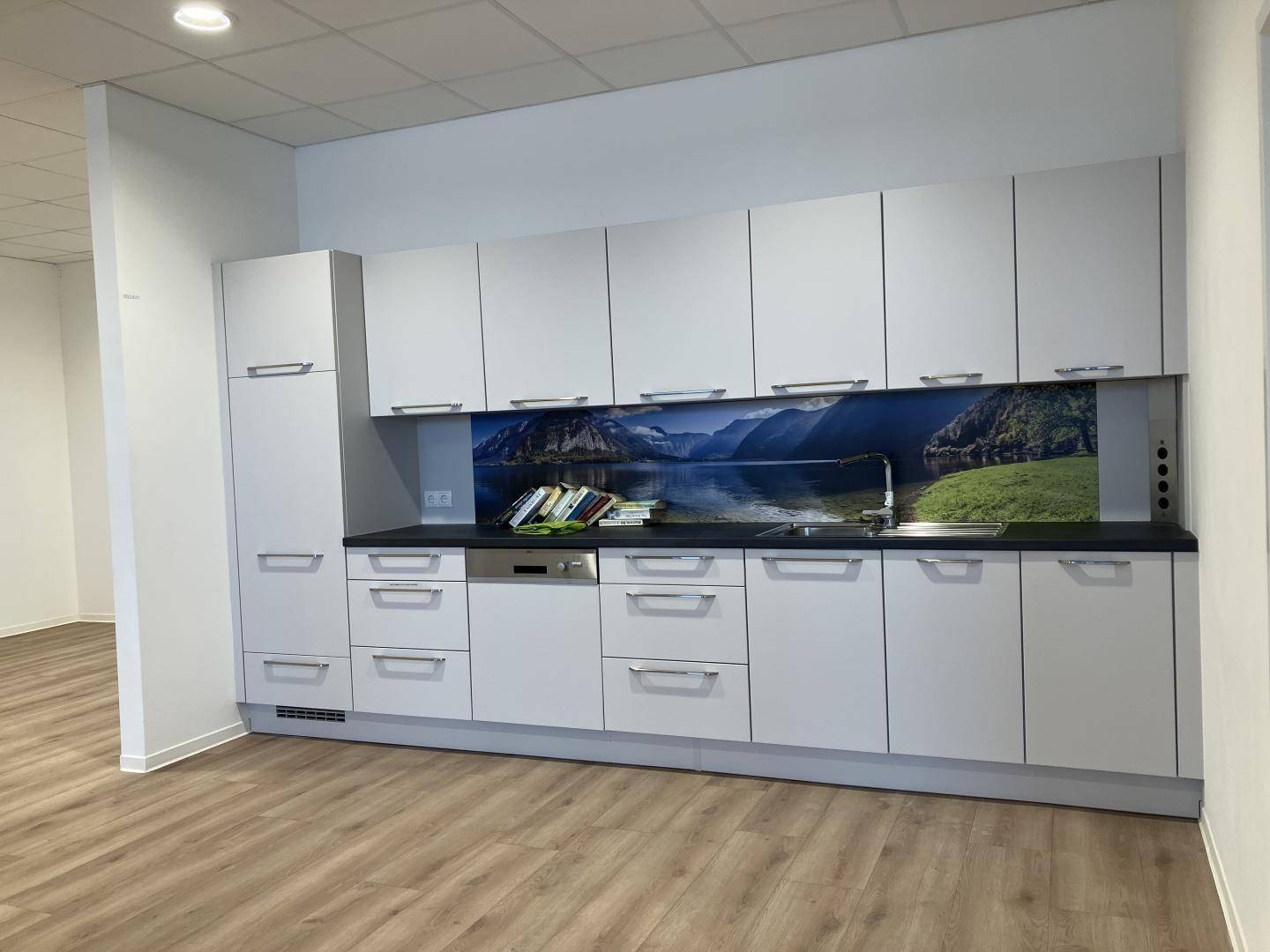 Moderne Teeküche mit weißen Schränken, Spülmaschine und einer dekorativen Rückwand.