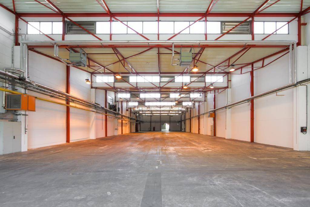 Geräumige Industriehalle mit hoher Decke, sichtbaren Trägern und Betonboden.